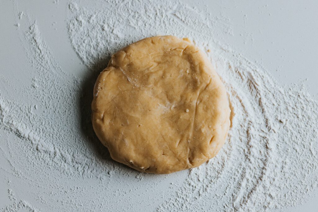 foto del panetto di pasta frolla su un piano da lavoro bianco, ricoperto di farina.